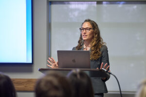 A woman stands at a podium presenting.